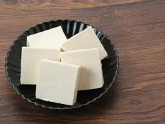 Kilka kostek białego tofu na czarnym talerzu. Czy tofu można mrozić? Tak, po rozmrożeniu zmienia teksturę, stając się bardziej gąbczaste.