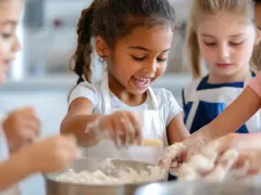 Des enfants joyeux préparent une recette dans des tabliers, les mains couvertes de farine.
