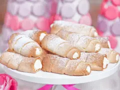 Domowe rurki z kremem, posypane cukrem pudrem, wyglądają apetycznie obok pastelowych dekoracji.
