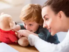 Uśmiechnięta opiekunka do dziecka bawi się z chłopcem pluszowym misiem.