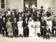 Un groupe pose pour une photo de mariage, peut-être pour un registre mariage. La mariée porte une robe blanche et un voile.