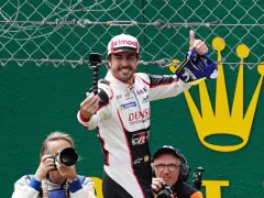 Fernando Alonso celebra su victoria en Le Mans, con una gorra y un trofeo. Fotógrafos capturan el momento.