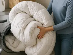 Persona mete un edredón blanco en la lavadora. Aprende como lavar un plumas a mano para mantenerlo esponjoso.