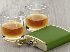 Zwei Gläser mit bernsteinfarbenem Whiskey und ein grüner Taschenflachmann. Ein 4 cl Whiskey hat ca. 90 Kalorien.