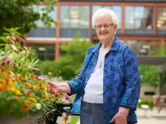 An elderly woman smiles, tending to flowers outside the St. Rose of Viterbo Convent.