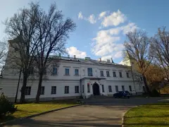 Pałac w Falentach, biała, okazała budowla z wieżyczką, otoczona drzewami o nagich gałęziach, pod błękitnym niebem z chmurami.