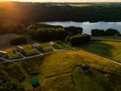 Malownicze domki nad jeziorem, idealne na fajne miejsca na wakacje. Słońce zachodzi, rzucając złote światło na pola i lasy.