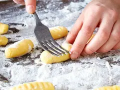 Hände formen mit einer Gabel die Rillen für original Gnocchi auf einer bemehlten Arbeitsfläche.