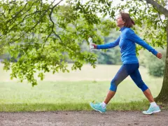 Femme souriante en tenue de sport bleue, profitant de 30 minutes de marche rapide par jour dans un parc verdoyant.