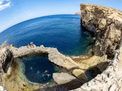 Ludzie kąpią się w naturalnym basenie skalnym, znanym jako blue hole, otoczonym klifami i turkusowym morzem.