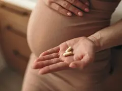 Dłoń ciężarnej kobiety trzyma dwie kapsułki. Lekarz zalecił ampicylinę na infekcję.