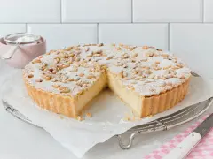Eine köstliche Torta della Nonna, bestäubt mit Puderzucker und Pinienkernen, wartet darauf, angeschnitten zu werden.