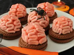 Gruselige Halloween-Nachspeise: Kekse mit Gehirn-förmiger rosa Glasur, dekoriert mit einer Spinne. Kerzen leuchten im Hintergrund.
