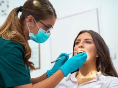 Dentystka w masce i rękawiczkach bada zęby pacjentki. To nie jest wyrywanie 8, ale rutynowa kontrola.