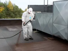Pracownik w białym kombinezonie aplikuje preparat na dach. To ważny etap prac, by zapewnić trwałość i szczelność dachu, chroniąc go przed wilgocią. Styropapa to materiał, który wymaga fachowej aplikacji.