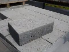 Stos szarych bloczków betonowych, każdy z widocznymi nierównościami i kruszywem. Wymiary bloczków betonowych są standardowe dla budowy.