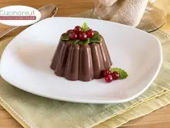 Budino al cioccolato decorato con ribes rossi e menta, servito su un piatto bianco.