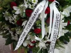 Wieniec pogrzebowy z białymi liliami i czerwonymi różami. Napis na szarfie: "Z ostatnim pożegnaniem od koleżanki i kolegów z Komendy Miejskiej Policji w Olsztynie".