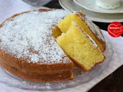 Una soffice torta allo yogurt, cosparsa di zucchero a velo, con due fette tagliate per mostrare la sua morbidezza. Perfetta per la colazione o la merenda.