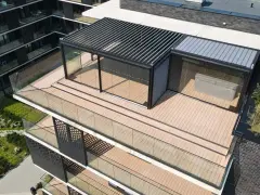 Nowoczesny taras na dachu z przeszklonym pawilonem i pergolą. Drewniana podłoga i szklane balustrady tworzą elegancką przestrzeń.