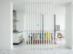 Elegante solución para dividir salón en dos ambientes. Cocina moderna y comedor con sillas de colores, separados por una celosía blanca.