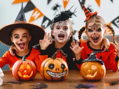 Tre barn med läskig ansiktsmålning och halloweenkostymer njuter av halloween aktiviteter med pumpor och dekorationer.