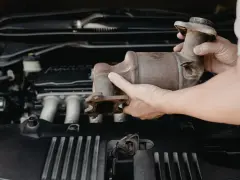 Mani che rimuovono un catalizzatore arrugginito dal vano motore di un'auto. Riparazione del fap auto.