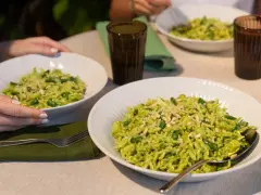 Due piatti di trofie al pesto, condite con fagiolini e pinoli, pronte per essere gustate.