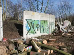 Graffiti-bemalte Überreste der Berliner Mauer, umgeben von Holzstapeln und Trümmern.