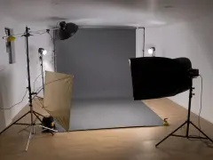Studio fotograficzne z szarym tłem, lampami i dyfuzorem. Światło kontrowe tworzy dramatyczne cienie.