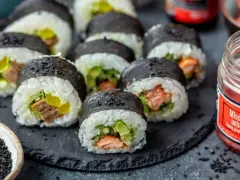 Gotowe sushi z łososiem i awokado, idealne do nauki jak zrobić sushi w domu. Obok słoiczek marynowanego imbiru.