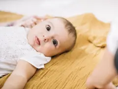 Niemowlę leży na musztardowym kocyku. Kiedy się niepokoić, gdy dziecko nie chodzi? Zwykle nie ma powodu do obaw, jeśli maluch rozwija się prawidłowo.