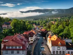 Widok na urokliwe miasteczko Szklarska Poręba z czerwonymi dachami, otoczone bujną zielenią i mglistymi Karkonoszami.
