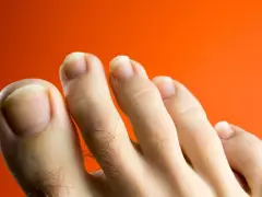 Primer plano de unos pies con uñas amarillas sobre fondo naranja.