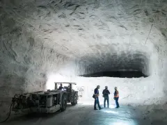 Wnętrze kopalni soli Kłodawa. Górnicy w hełmach i kamizelkach obserwują pracę maszyny wydobywczej w białej, solnej grocie.