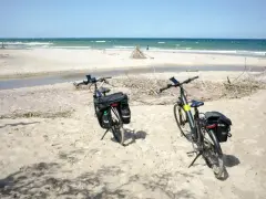 Dwa rowery z sakwami na piaszczystej plaży, gotowe na odkrywanie tras rowerowych nad morzem.