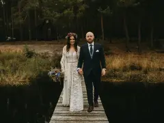 Para idzie przez las, ona w koronkowej sukni i wianku, on w garniturze. Ich suknia ślubna boho rustykalna idealnie pasuje do leśnej scenerii.