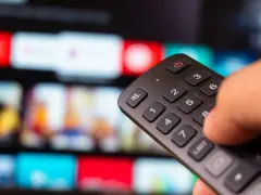 Dłoń trzyma pilot do telewizora, wybierając film na ekranie. To idealny moment na relaks z web tv.