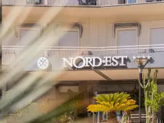 Hotel Nord Est sign with a compass logo and five stars, framed by palm fronds.