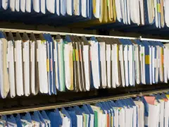 Rzędy wiszących segregatorów, gotowych do archiwizacji dokumentów. Widać tu wiele teczek, niektóre z kolorowymi etykietami, idealne do organizacji pracy, np. z wykorzystaniem systemu druk erp-6.