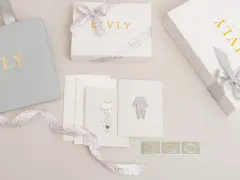 En nyfödd present box från Livly Stockholm med en grå påse, vita boxar med guldig text och leopardmönstrat band. Kort med illustrationer av en elefant och en babybody.