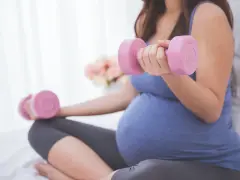 Ciężarna kobieta wykonuje ćwiczenia z hantlami, przygotowując się do porodu.