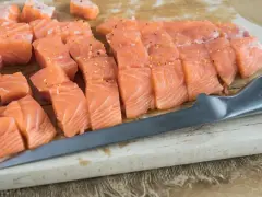 Świeży, pokrojony łosoś do sushi, doprawiony, leży na desce obok noża. Idealny łosoś do sushi.