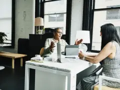 Dos mujeres discuten sobre el impuesto de sociedades y contabilidad en una oficina moderna.