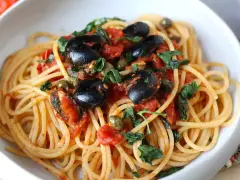 Un piatto invitante di spaghetti alla puttanesca, con olive nere, capperi e pomodoro fresco, guarnito con prezzemolo.