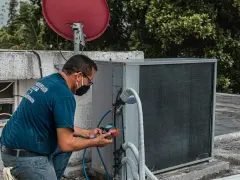 Technik sprawdza czujnik ciśnienia klimatyzacji, podłączając manometr do jednostki zewnętrznej.