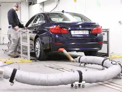 Blauer BMW auf einem Prüfstand für Abgastests. Ein Techniker überwacht die Messungen, die für die Euro 6-Abgasnorm relevant sind.