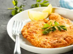 En gyllene schnitzel med citronklyfta och persilja, redo att avnjutas med ett glas vin till schnitzel.