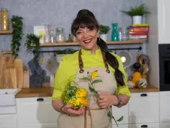 Cristina Catese w kuchni, trzymająca ozdobną dynię i słonecznik.