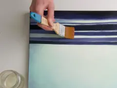 Main d'artiste appliquant une couche de vernis sur une toile aux rayures bleues et blanches. Quel vernis !